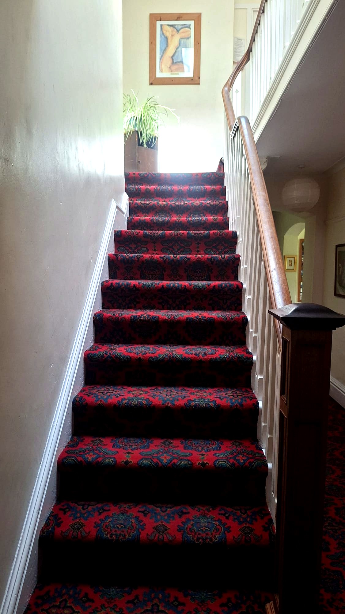 Staircase with patterned red runner leading up to a bright landing